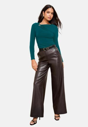 Teal långärmad topp med rynkning och silverdetaljer, kombinerad med högmidjade bruna vida läderbyxor och svarta klackar med remmar.