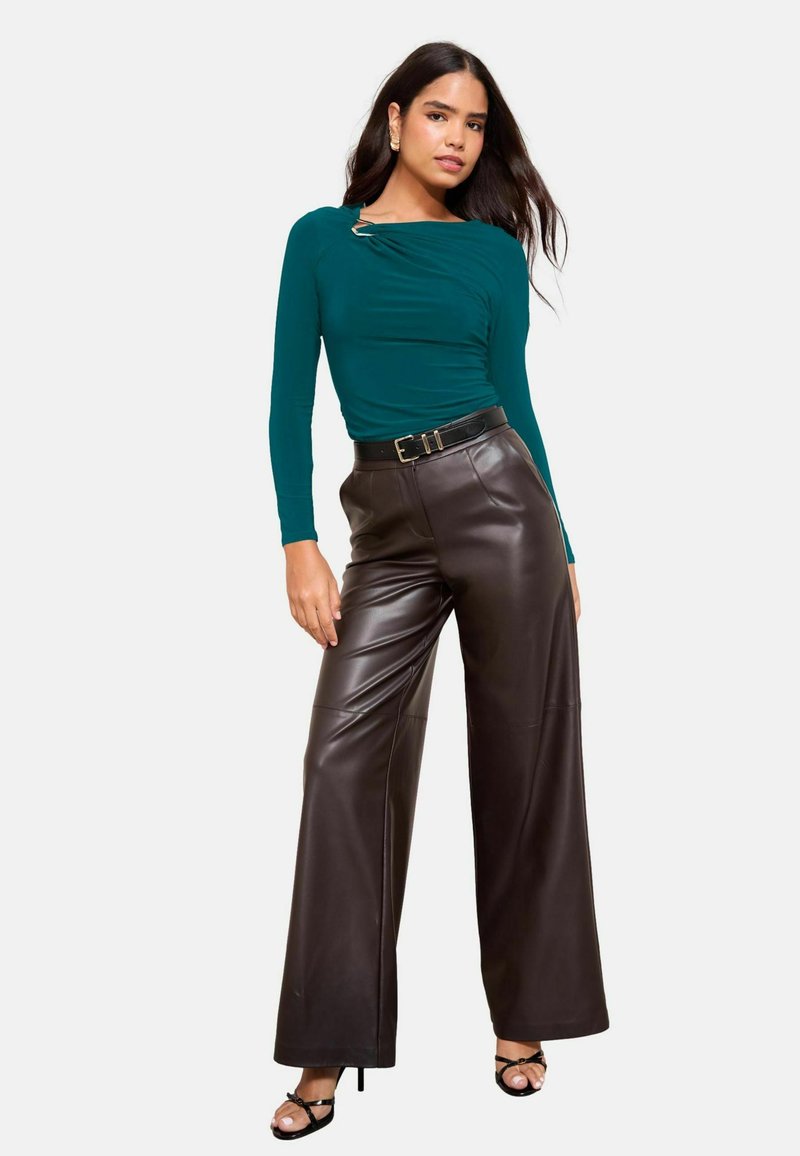 Tīrā zilganzaļa ilgo piedurkņu blūze ar krokām un sudraba detaļām, apvienota ar augsto vidukli brūnām platām ādas biksēm un melnajām siksnu kurpēm ar augstiem papēžiem.