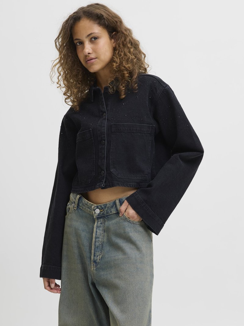 Svart cropped denimjacka med knäppning, framfickor och subtila detaljer, kombinerad med ljusblå vida jeans.
