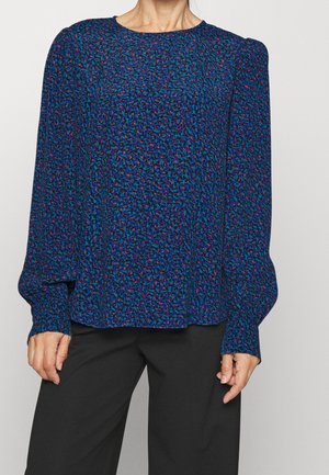 Blusa blu con texture, colletto rotondo e maniche lunghe, caratterizzata da un motivo a chiazze multicolori. Abbinata a pantaloni neri.