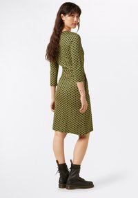 Vihreä ja keltainen kuvioitu mekko, jossa on kolme neljännesosaa hihoista, vyötärö on suora ja A-linjainen hame, yhdistetty mustiin nauhakenkiin.