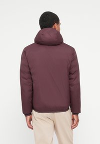 Chaqueta de plumas burdeos con capucha, con una textura suave, puños elásticos y un corte ligeramente más corto en el dobladillo. Diseño minimalista.
