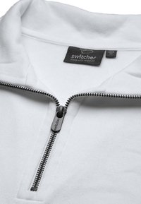 Pullover bianco con zip realizzato in tessuto morbido, presenta un colletto alto e una zip nera con il marchio "switcher" sul tirante.