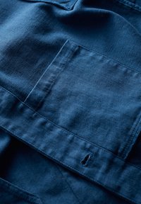 Navy blue fabric, featuring a smooth texture and herringbone pattern, with a patch pocket and a small hole near the bottom edge.