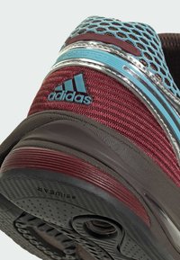 Rode en grijze Adidas sportschoen met een mesh bovenzijde, gestructureerde stof, zilverkleurige accenten en een patroon van rubberen zool.