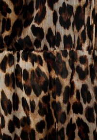 Tkanina s leopard uzorkom koja prikazuje velike, nepravilne crne i smeđe mrlje na svijetloj bež pozadini s teksturiranom površinom.