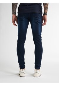 Tmavě modré skinny džíny vyrobené z denimu, s zadními kapsami, lehkým vyblednutím a kombinované s bílými teniskami.