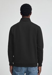 Felpa nera con colletto alto, maniche lunghe e vestibilità comoda. Presenta polsini a costine e orlo dritto, abbinata a jeans azzurri chiari.