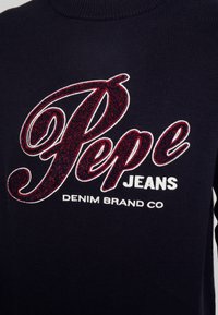 Maglione lavorato a maglia blu navy con logo "Pepe Jeans" in rosso e contorno bianco. Il materiale è morbido, con una texture a coste e un design aderente.