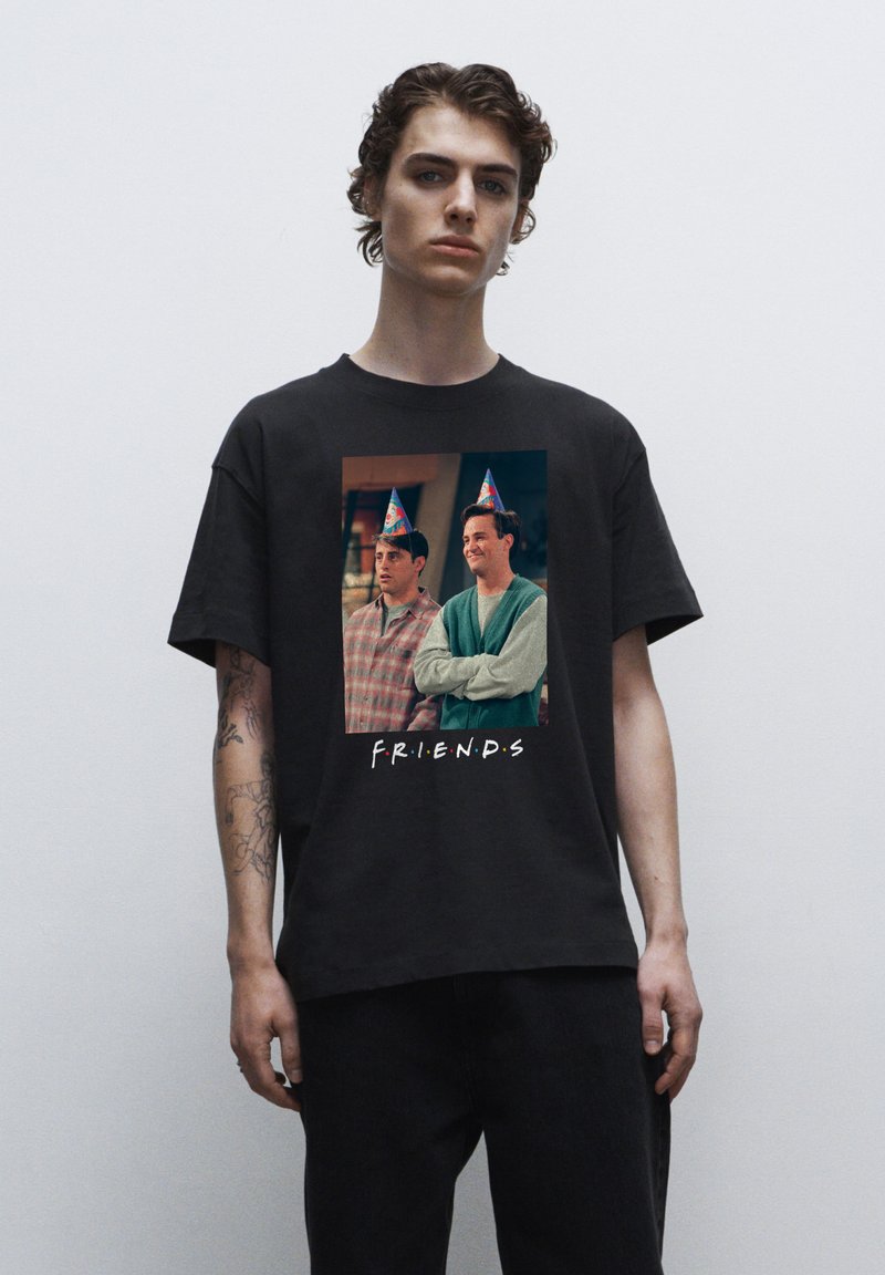Černé tričko s grafikou ztvářující dvě postavy v party kloboucích z televizního pořadu, obklopené textem "F.R.I.E.N.D.S."