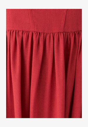 Robe en tissu rouge avec une surface texturée, comportant un corsage ajusté et une jupe ample et froncée avec des plis verticaux.