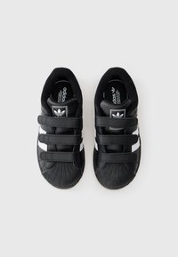 Schwarze Sneaker mit drei Klettverschlüssen, weißen Akzentstreifen und einer strukturierten Gummikappe. Mit Adidas-Logo auf der Zunge.