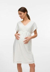 Robe de maternité blanche avec un décolleté en V, des manches courtes et une taille à cordon. Présente un motif ajouré texturé sur l'ensemble. Tissu lisse.
