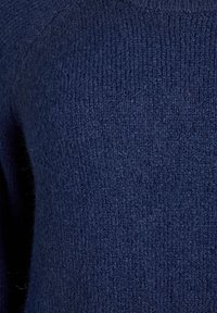 Granatowy sweter z dzianiny z teksturowanym wzorem i miękkim, puszystym wykończeniem. Zbliżenie na materiał bez widocznych szwów lub akcentów.
