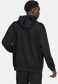 Svart huvtröja med ribbat mönster, avslappnad passform och framficka i kengurustil. Har en luvtröja med dragsko och muddar vid ärmarna.