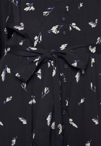 Črna obleka s cvetličnim vzorcem v beli in modri barvi, z gumbnim zapenjanjem spredaj in pasom iz tkanine. Mehka tekstura.