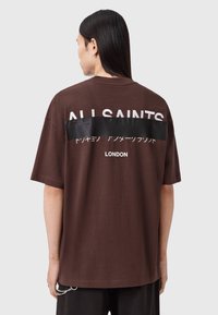 Braunes Baumwoll-T-Shirt mit einem großen weißen "ALL SAINTS"-Logo, einem schwarzen Grafikpanel und dem Schriftzug "LONDON" auf der Rückseite. Kurze Ärmel und lockere Passform.