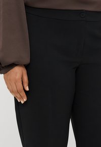 Schwarze Hose aus glattem Stoff mit einem Knopfverschluss auf der Taille. Sie hat eine schmale Passform und eine Seitennaht-Tasche.