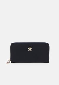 Navy blue zip-around wallet made of smooth material, featuring a gold logo on the front, with a contrasting tag on the zipper pull.