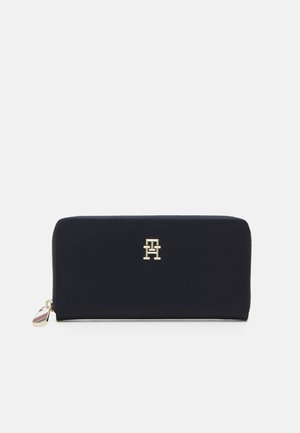 Portafoglio blu navy con zip, realizzato in materiale liscio, caratterizzato da un logo dorato sul fronte e un'etichetta a contrasto sul tirazip.