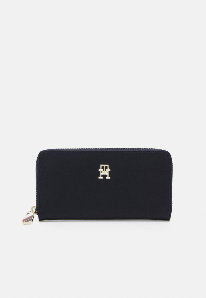 Navy blue zip-around wallet made of smooth material, featuring a gold logo on the front, with a contrasting tag on the zipper pull.