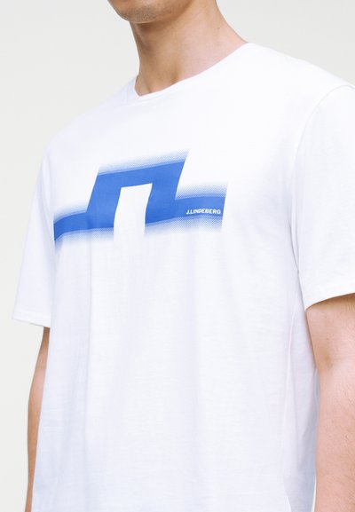 Λευκό βαμβακερό T-shirt με μπλε γραφικό σχέδιο στο μπροστινό μέρος. Κοντά μανίκια και στρογγυλή λαιμόκοψη. Όνομα εμπορικής φίρμας σε μικρή εκτύπωση.