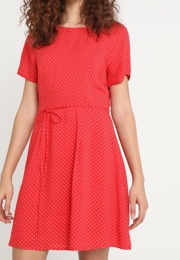 Robe rouge à manches courtes avec des pois blancs, taille cintrée avec un lien, jupe évasée et tissu à la texture lisse.
