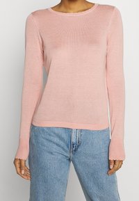 Rosa långärmad tröja med rundad halsringning, ribbad textur och vågig nederkant. Kombinerad med ljusblå denimjeans.