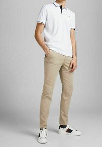 Polo bianco con dettagli blu navy, pantaloni beigi slim-fit e sneakers bianche con strisce rosse e blu navy. Design minimalista, vestibilità casual.