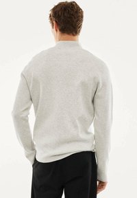 Hellgrauer Rundhals-Sweatshirt mit langen Ärmeln und lockerem Schnitt. Sanfte Textur, minimalistisches Design und gerippte Bündchen.