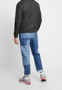 Svart vadderad bomberjacka med ribbade mudd och nederkant; blå patchwork denimjeans; grå sneakers med röda inslag; vita strumpor.