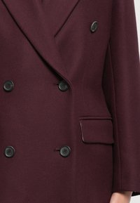 Burgunderfarbener, doppelt knöpfbarer Blazer aus strukturiertem Stoff, mit schwarzen Knöpfen, einer einzelnen Brusttasche und maßgeschneiderten Revers.