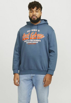 Blauwe katoenen hoodie met een trekkoordkap, voorzien van witte en oranje tekst op de borst. Gecombineerd met lichtblauwe spijkerbroek.