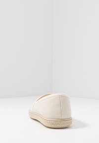 Beige kanva liukukengät pyöristetystä takaa, tikatut saumat ja teksturoitu juuttinarupohja. Yksinkertainen ja neutraali muotoilu.