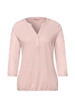 Blouse rose clair à manches longues avec trois boutons sur le devant, encolure ronde avec une fente en forme de V, poignets et ourlet élastiques.