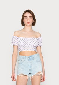 Top cropped de flores roxas com ombros à mostra e mangas bufantes, combinado com calções de ganga azul claro desgastados.