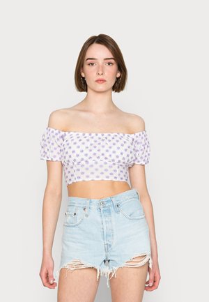 Top cropped de flores roxas com ombros à mostra e mangas bufantes, combinado com calções de ganga azul claro desgastados.