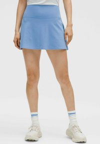 Svijetloplava aktivna suknja s prilagođenim pojasom, izrađena od glatkog materijala. Ima lepršavi dizajn i uparena je s bijelim tenisicama i prugastim čarapama.