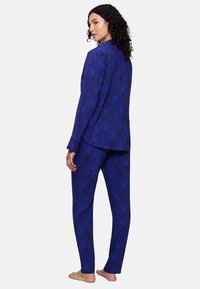 Navyblauw pyjamastel met ingewikkelde bloemenpatronen, gemaakt van zachte stof. Het bovenstuk heeft lange mouwen; de broek is recht en heeft een volledige lengte.