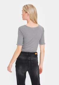 T-shirt grigia a coste con maniche corte a volant, abbinata a jeans neri a vita alta con tasche posteriori e una patch in pelle con il logo.