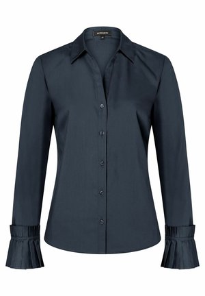 Chemise bleu marine foncé à manches longues avec boutons, col pointu et détails plissés sur les poignets des deux manches.