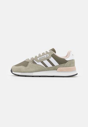 Adidas sneaker i olivengrøn og beige med hvide striber, snørebånd foran og lyserød detalje på hælen, vist fra siden på hvid baggrund.