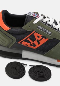 Zapatilla verde y negra con materiales de malla y ante, acentos naranjas y un detalle de logo. Incluye dos cordones negros.