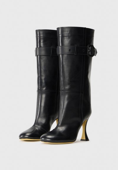 Black mid-calf leather boots with rounded toes, decorative straps and buckles near the top, and curved high heels with light-colored soles.