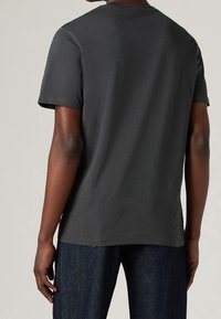 Tmavě šedé bavlněné tričko s kulatým výstřihem, krátkými rukávy a volným střihem. Má jednoduchý design bez viditelných vzorů nebo akcentů.