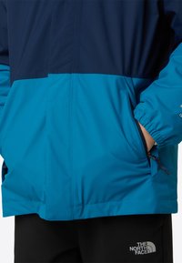Jachetă rezistentă la apă, cu design color-block în nuanțe de bleumarin și teal, cu manșete elastice și buzunare laterale pentru confort.
