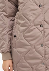 Kurtka pikowana w miękkim taupe o gładkiej fakturze. Posiada zatrzaski i boczną kieszeń. Projekt dopełniają mankiety na rękawach.