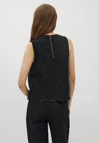 Zwarte mouwloze top met een scalloped zoom, cirkelvormige borduursels en een ritssluiting aan de achterkant. Soepele textuur, minimalistisch ontwerp.