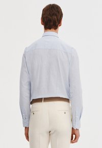 Jasnoniebieska lniana koszula o skróconym kroju. Posiada kołnierzyk z zapięciem na guziki oraz długie rękawy z regulowanymi mankietami.