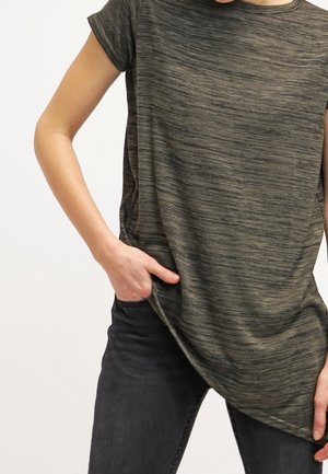Koszulka z krótkim rękawem w ciemnym oliwkowym kolorze, z melanżową teksturą i subtelnym zaokrągleniem u dołu. Połączona z ciemnymi dżinsami.